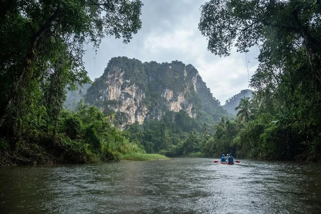 Kayakers on a jungle river beneath a limestone mountain framed by trees