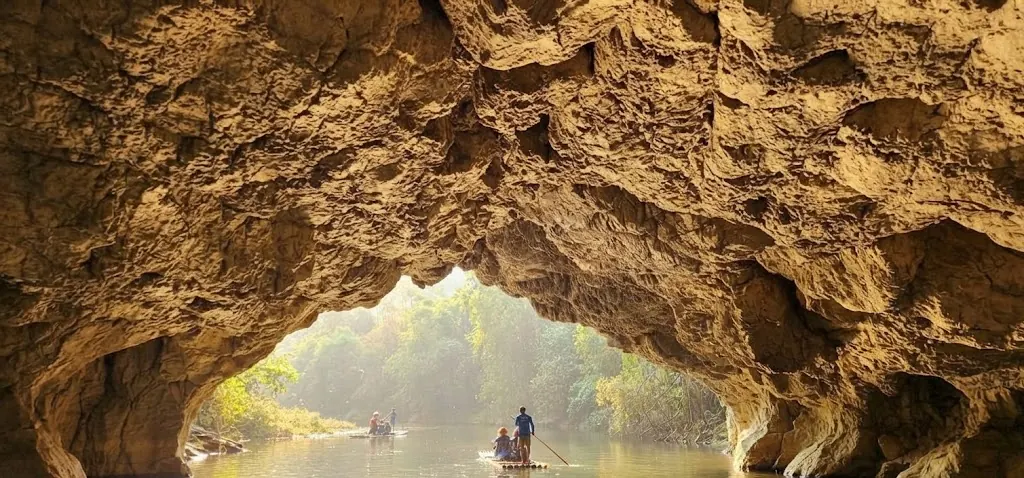 Limestone cave arch framing a jungle river and a small raft