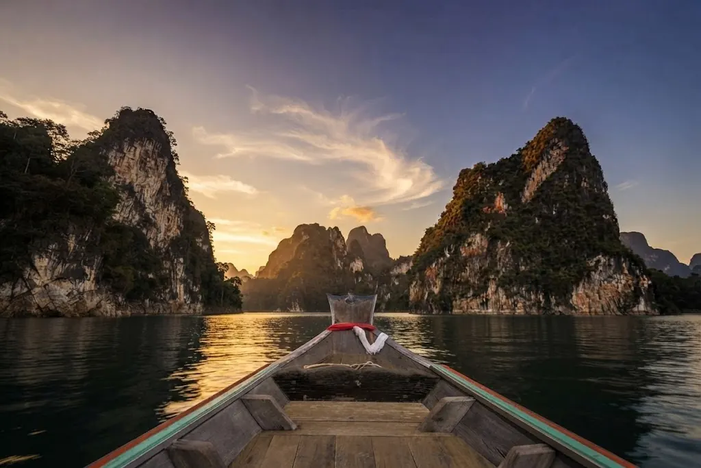 Long-tail boat bow heading between karst peaks at sunset