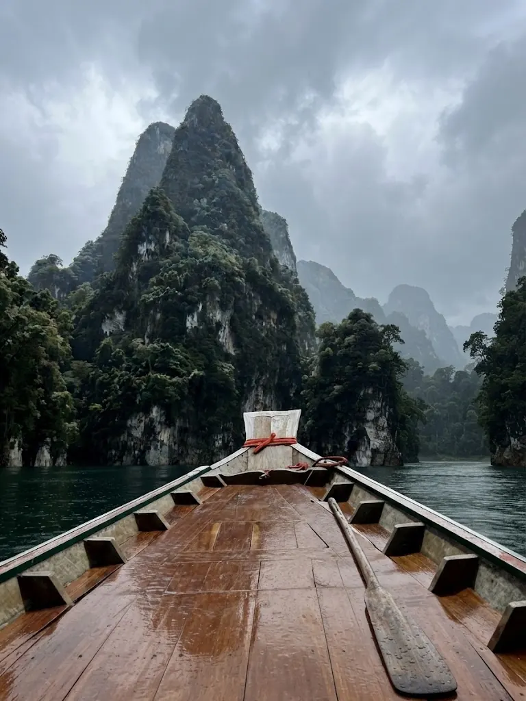 Long-tail boat bow pointing toward a steep karst peak under a grey sky