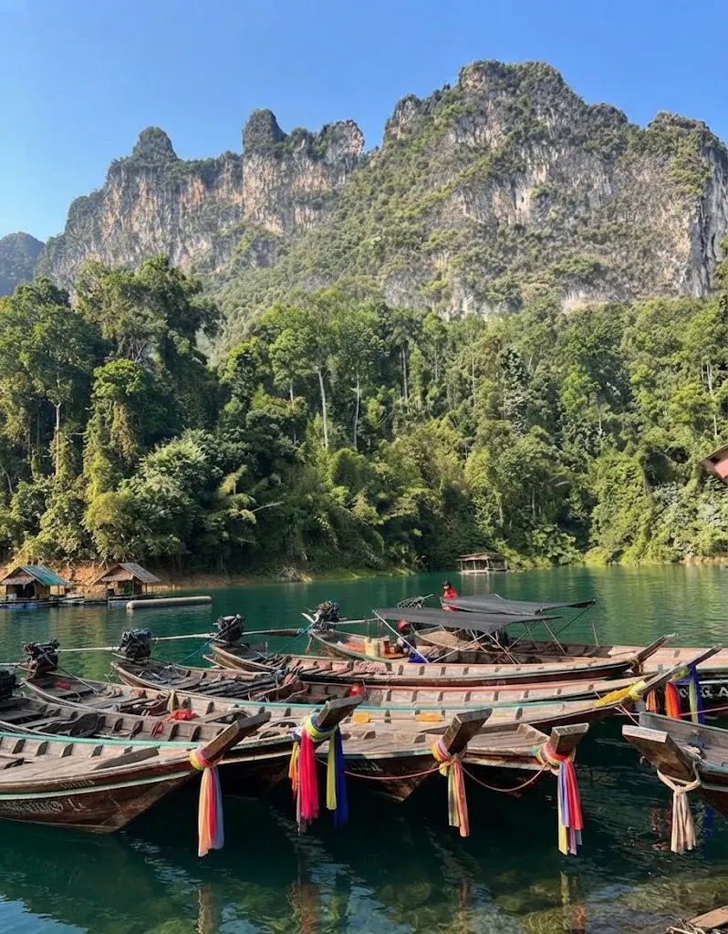 Long-tail boats moored at a pier beneath a jagged limestone ridge
