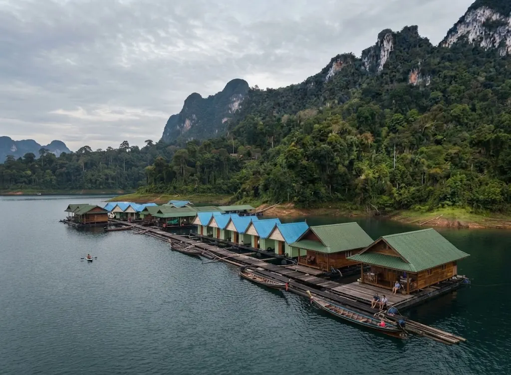 Row of green-roofed floating raft houses moored along a forested shore of Cheow Lan Lake